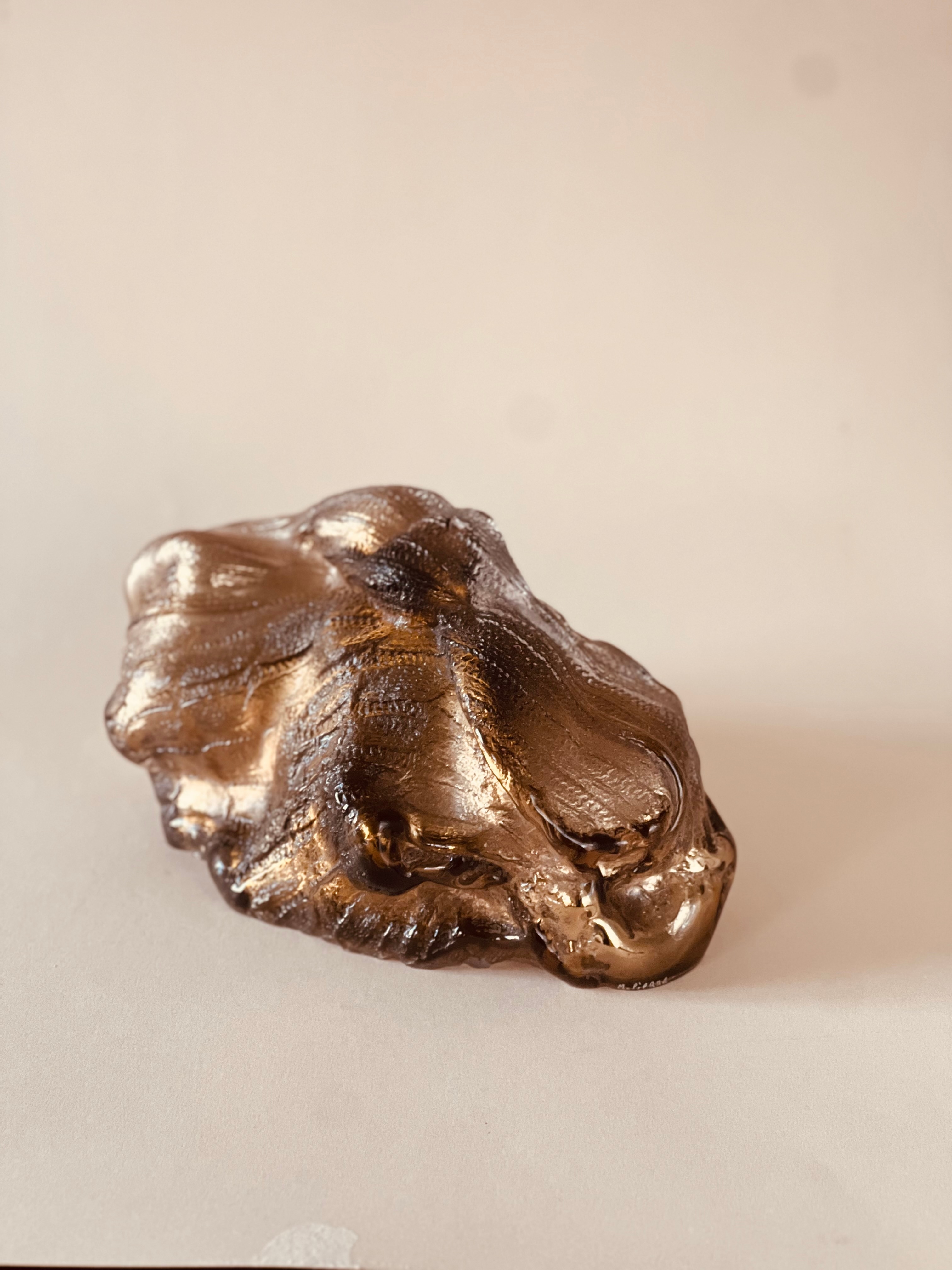 The sculpture Anthozoa: a low, smoky bronze glass form with puffed, knitted-textured folds and silvery highlights, lying on a pale surface.