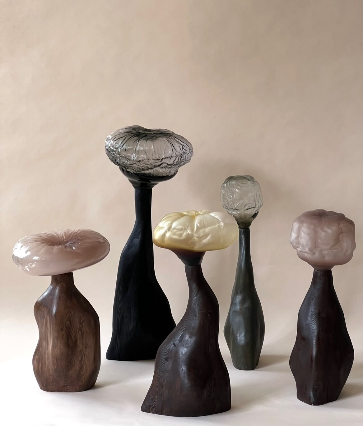 Spira / Sprout: five glass-topped sculptures on carved dark wooden bases on a pale pink backdrop.