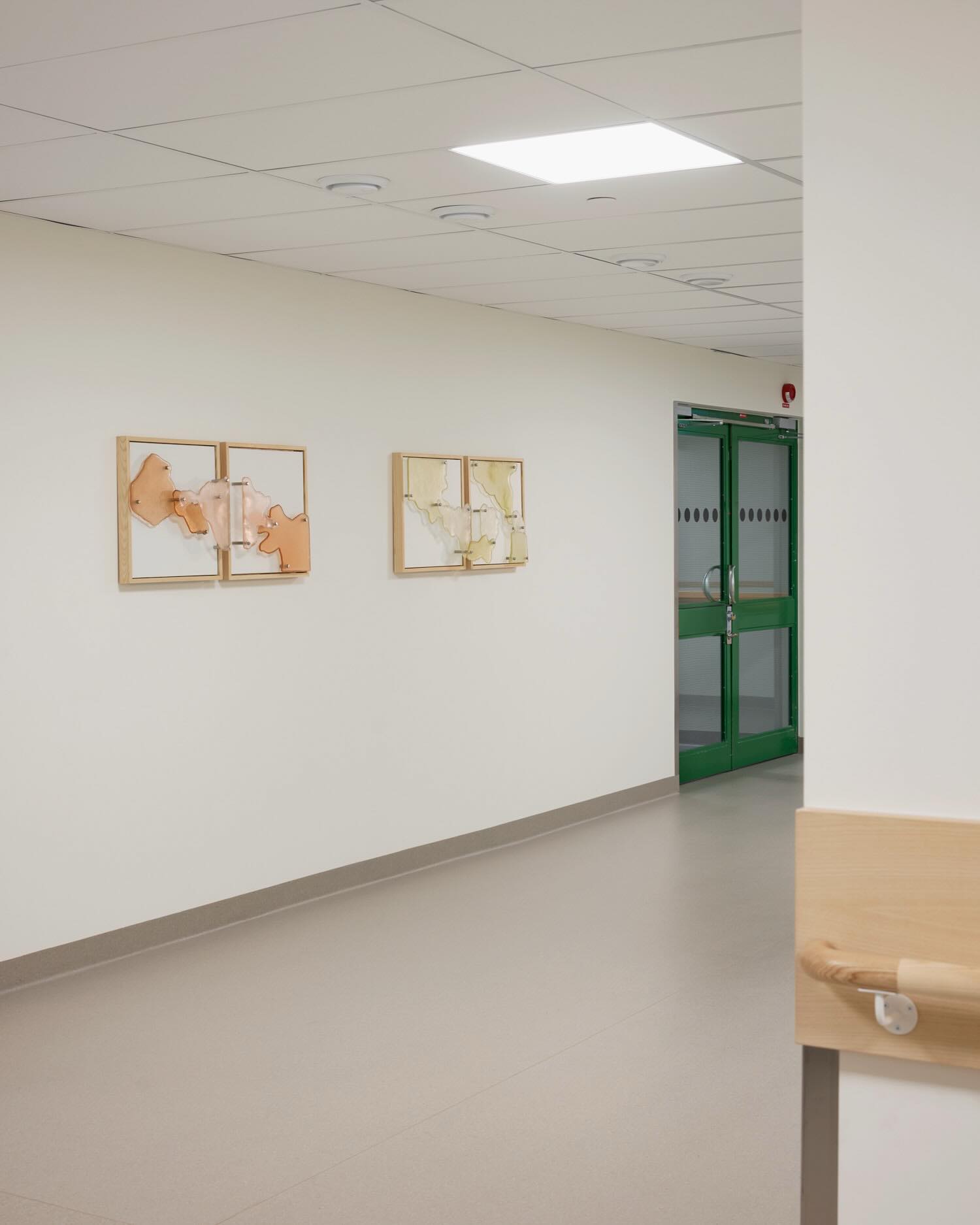 A hospital corridor in Eskilstuna with the diptychs Minnets geografi and Inre karta on a white wall.